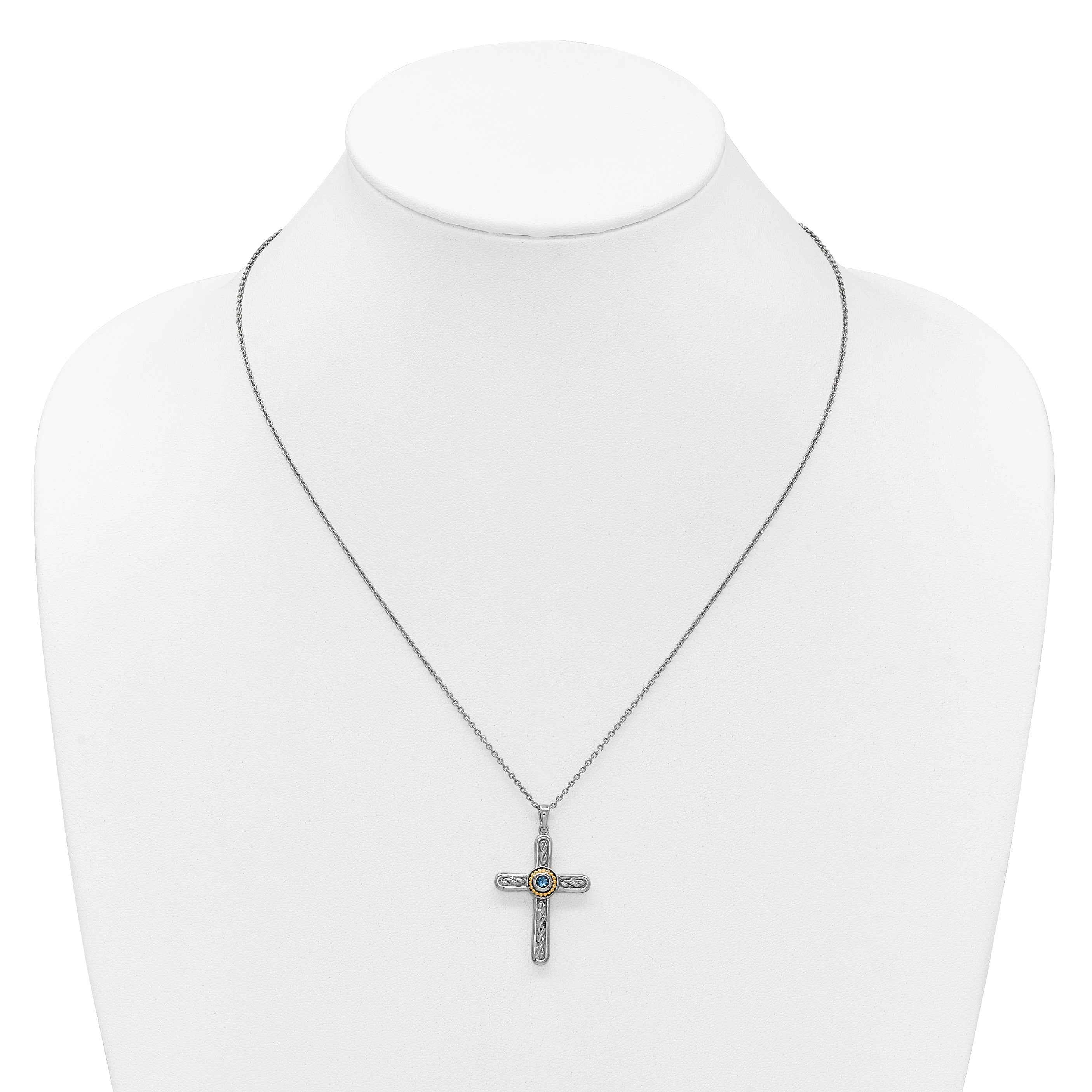 Silver cross necklace with blue gemstone center on white display bust
